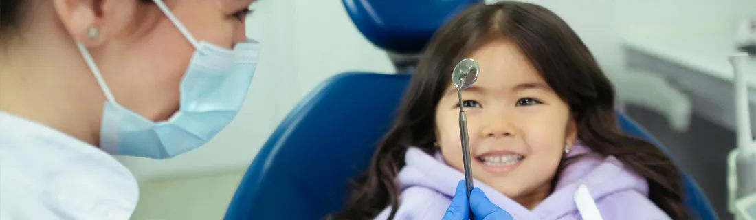 Dentist Muncie IN 5 Signs Your Child May Need Pedicatric Denal Care A little girl with dark hair sitting in a dental chair smiling at assistant holding a tool